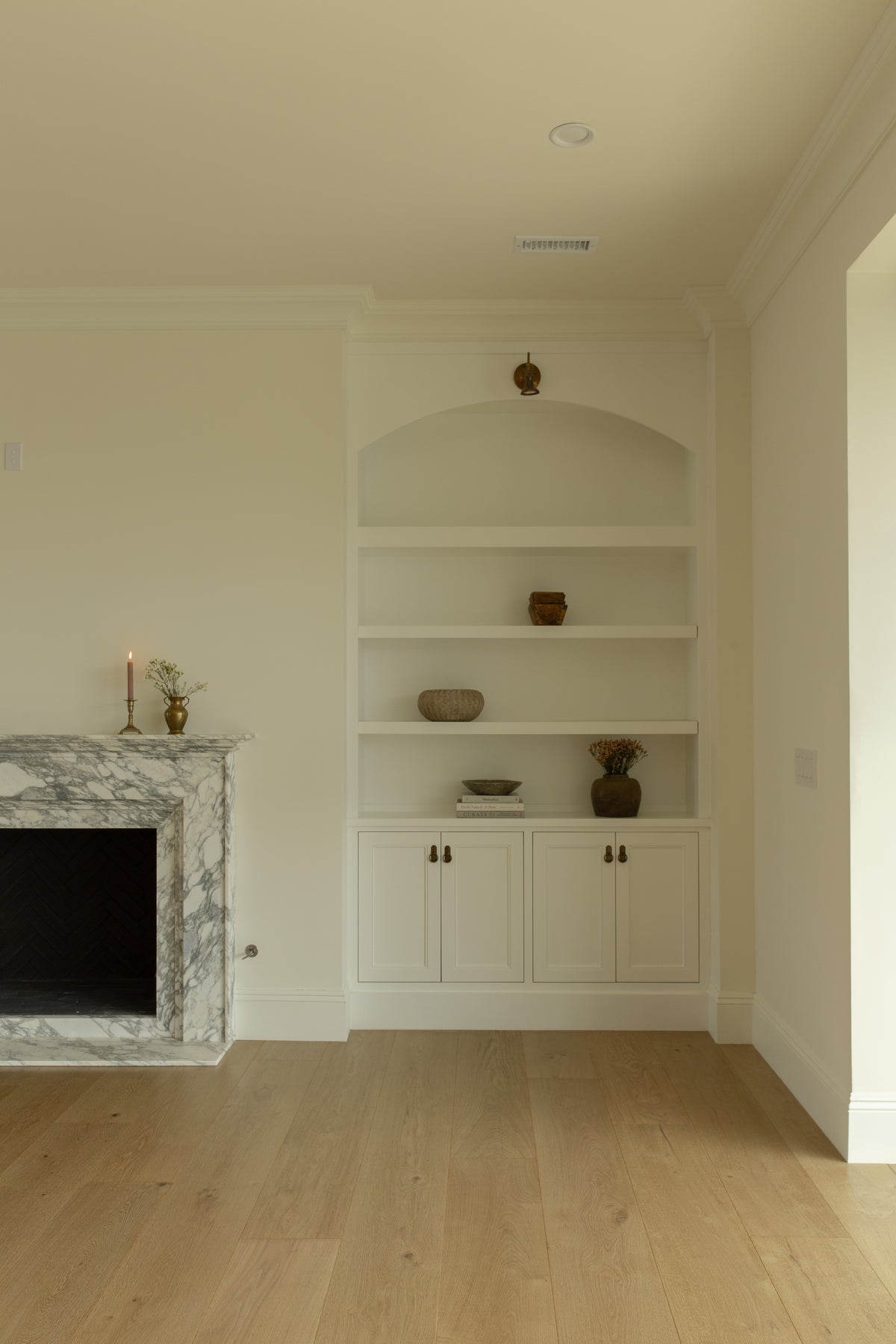 Custom white built-in shelving with an arched top and lower cabinets, positioned gracefully next to a marble fireplace in a Rossmoor home.
