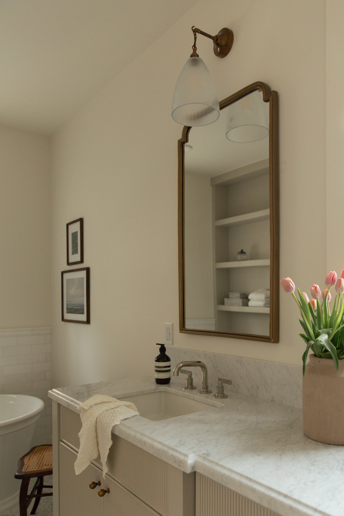 A beautifully styled vanity area showcasing a custom marble countertop, an elegant brass arched mirror, and a vintage-inspired fluted glass wall sconce.