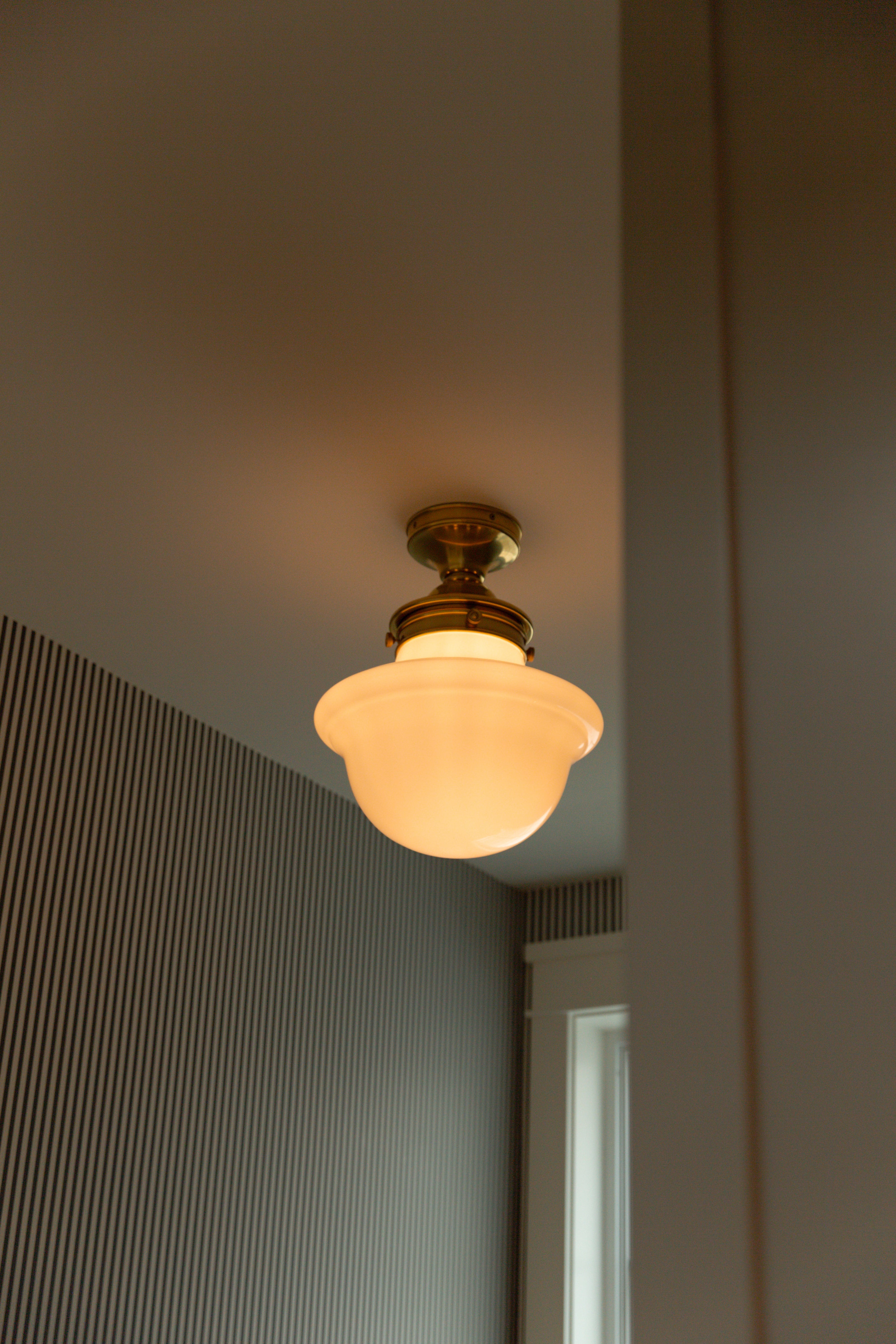 Close-up of a vintage-inspired brass and milk glass flush mount light fixture set beautifully against classic black and white striped wallpaper.