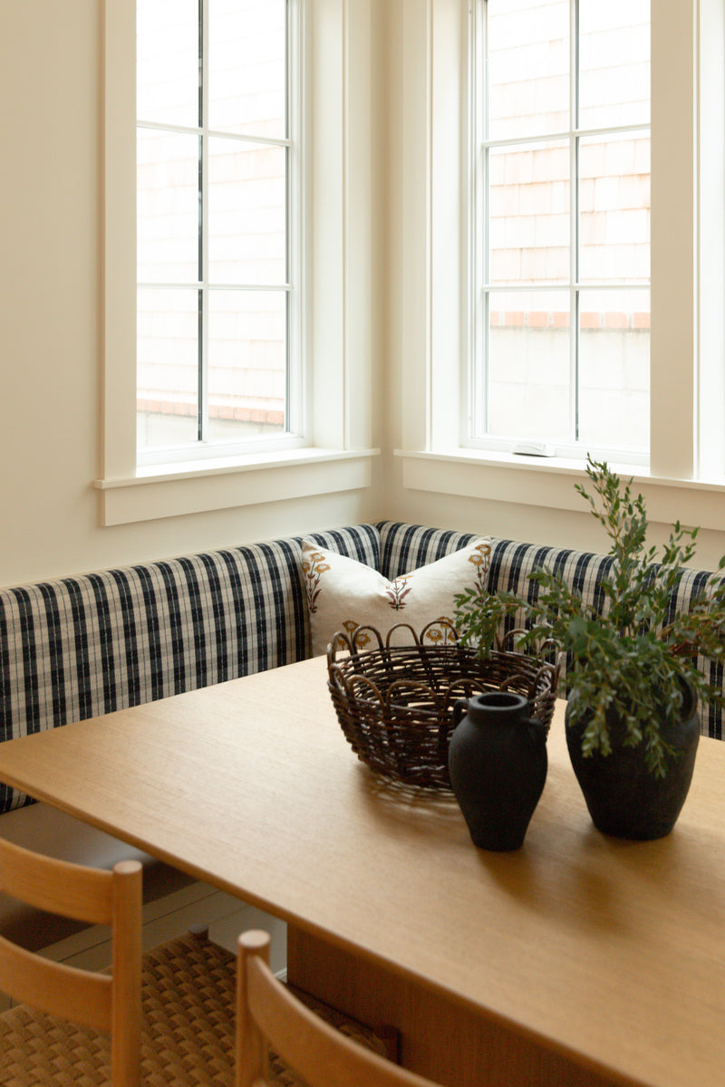 A cozy coastal farmhouse breakfast nook featuring custom built-in banquette seating with blue plaid upholstery and a light oak dining table.