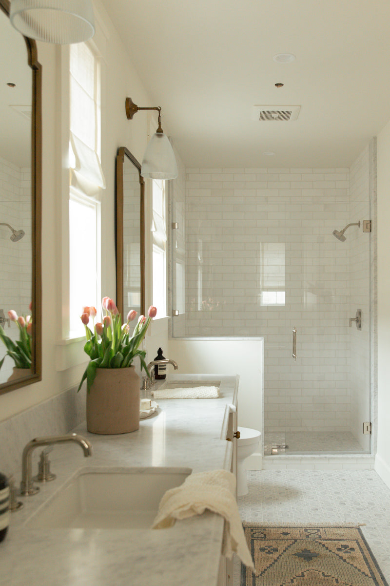 A luxurious primary bathroom design featuring a long double vanity, patterned tile flooring, and a seamless glass-enclosed walk-in shower finished with white subway tile.