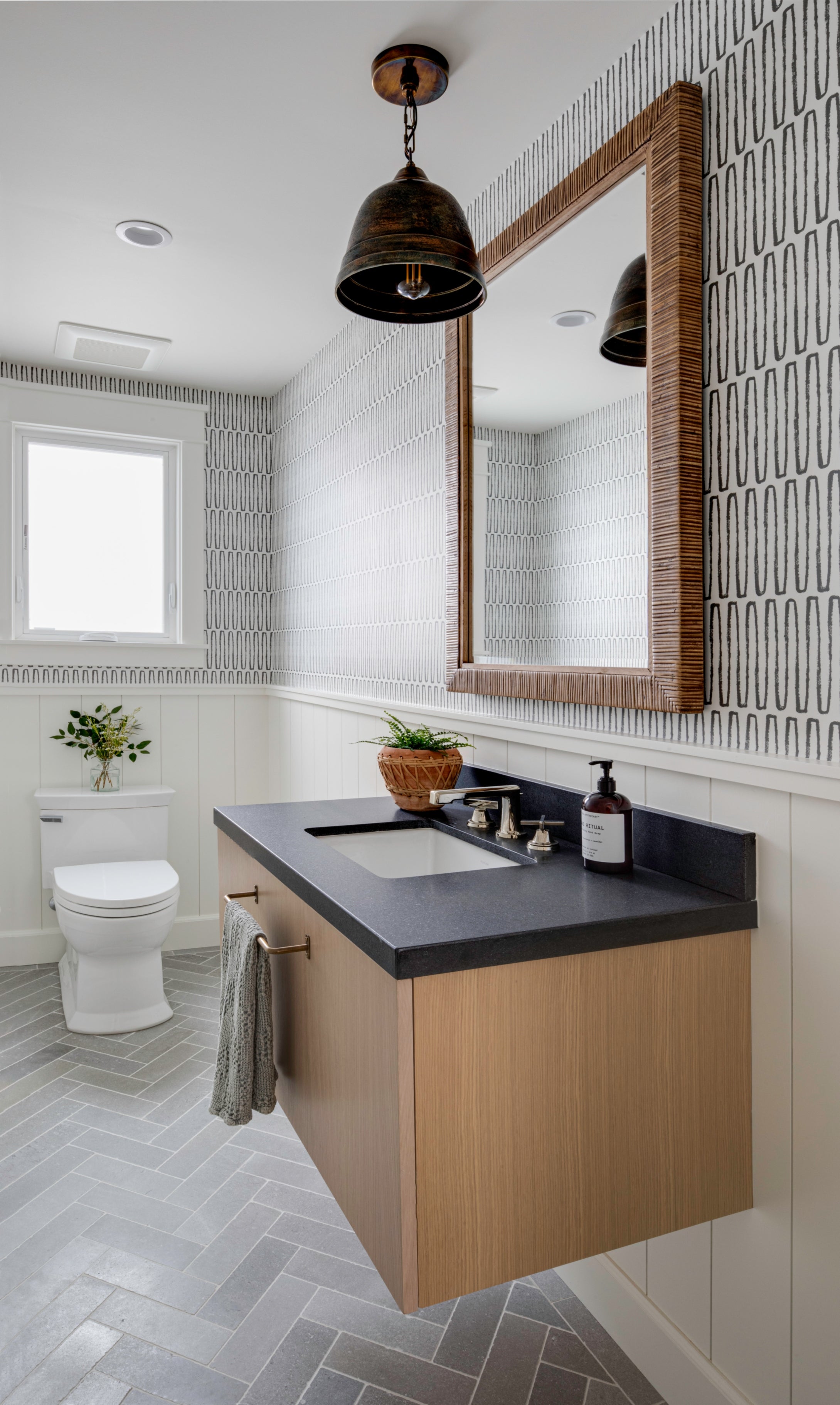 Transitional bathroom design with beadboard wainscoting, a rattan-framed mirror, and a unique metal pendant light fixture.