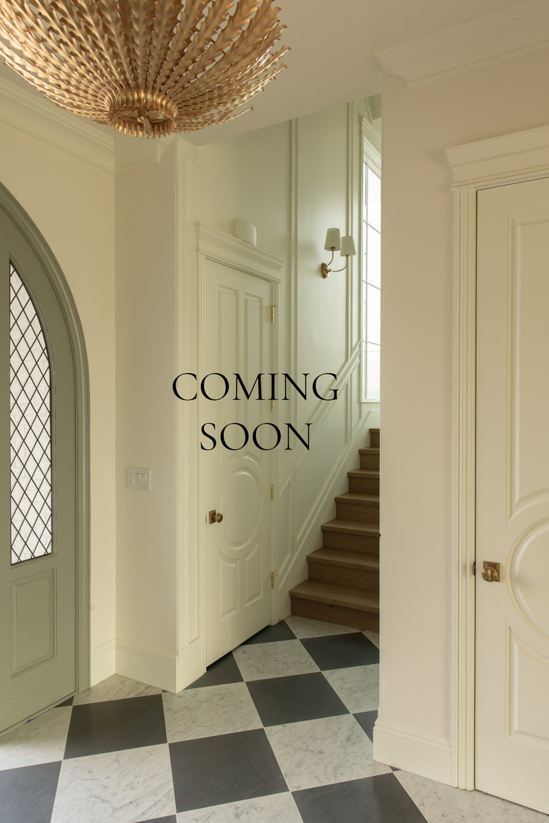 Teaser image with the text "COMING SOON" overlaid on an elegant entryway in a Rossmoor residential design project, featuring black and white marble checkerboard flooring, an arched front door with diamond glass, and a statement gold chandelier.