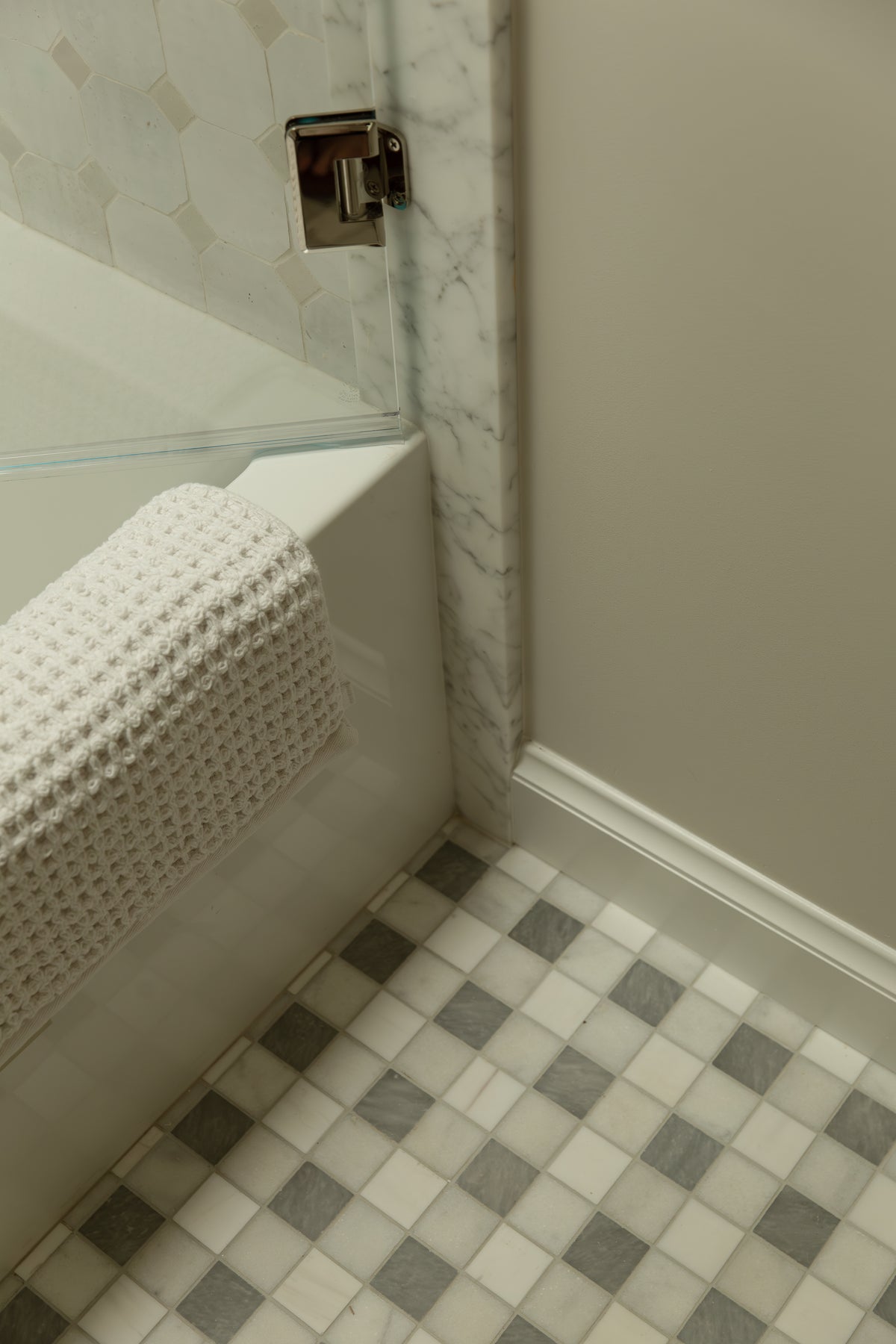 High-end crafted bathroom design featuring natural marble trim, custom-cut baseboards, and a vintage-style glass door enclosure, demonstrating meticulous architectural detail.
