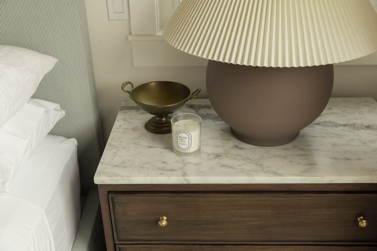 Close-up of a dark wood nightstand with a marble top, ceramic lamp with pleated shade, and brass bowl in a Craftsman bedroom design.