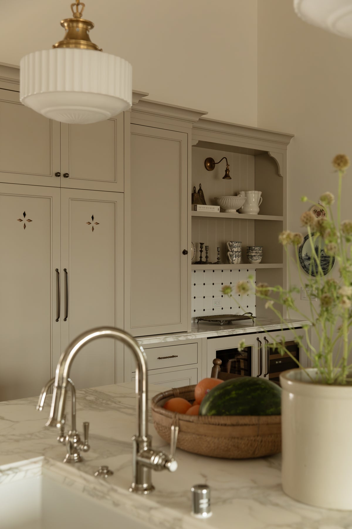 Kitchen island perspective showing a nickel faucet, ribbed glass pendant light, and background built-in hutch cabinetry with open shelving.