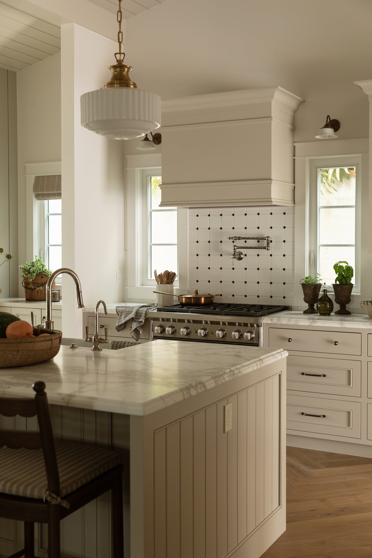 View from the kitchen island featuring vertical beadboard side paneling, brass pendant lighting, herringbone wood floors, and a gas range setup.