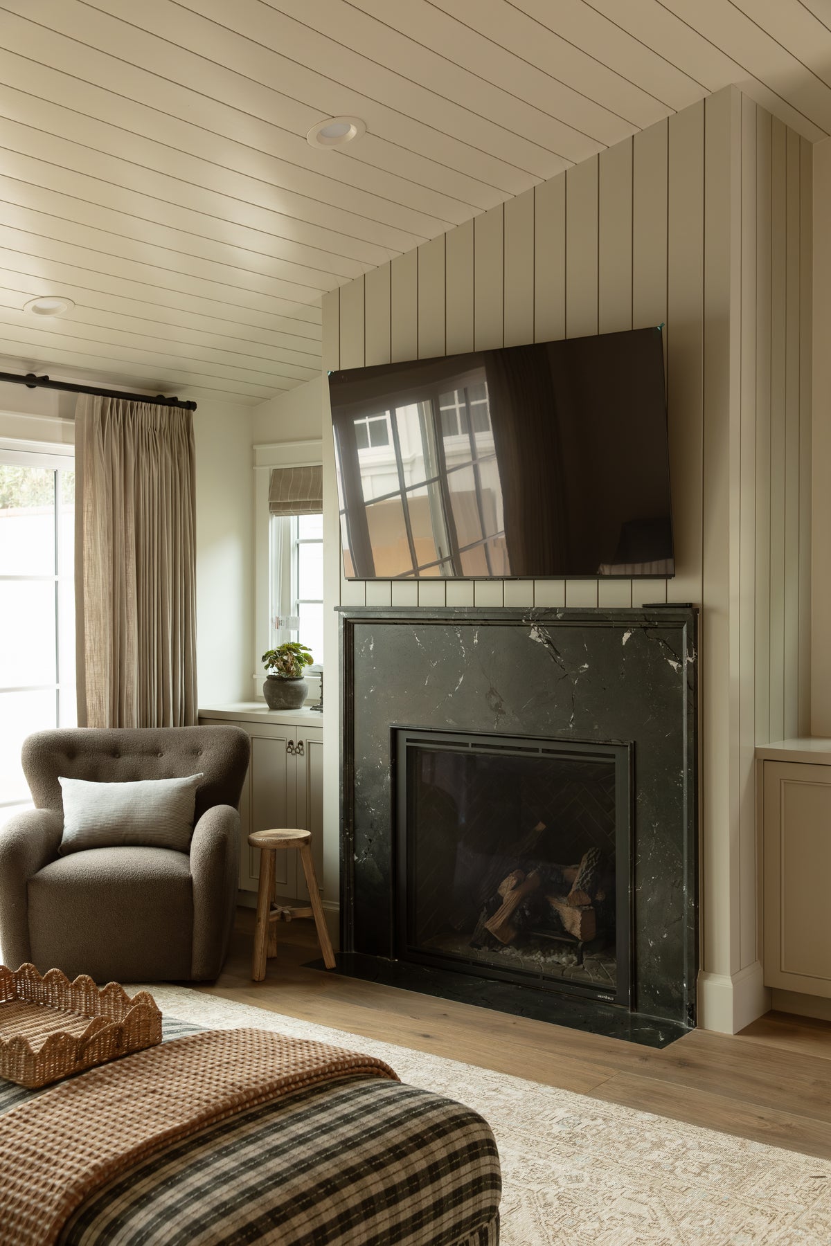 Living room corner with a black marble fireplace surround, vertical paneling detail, wall-mounted TV, and cozy upholstered armchair.