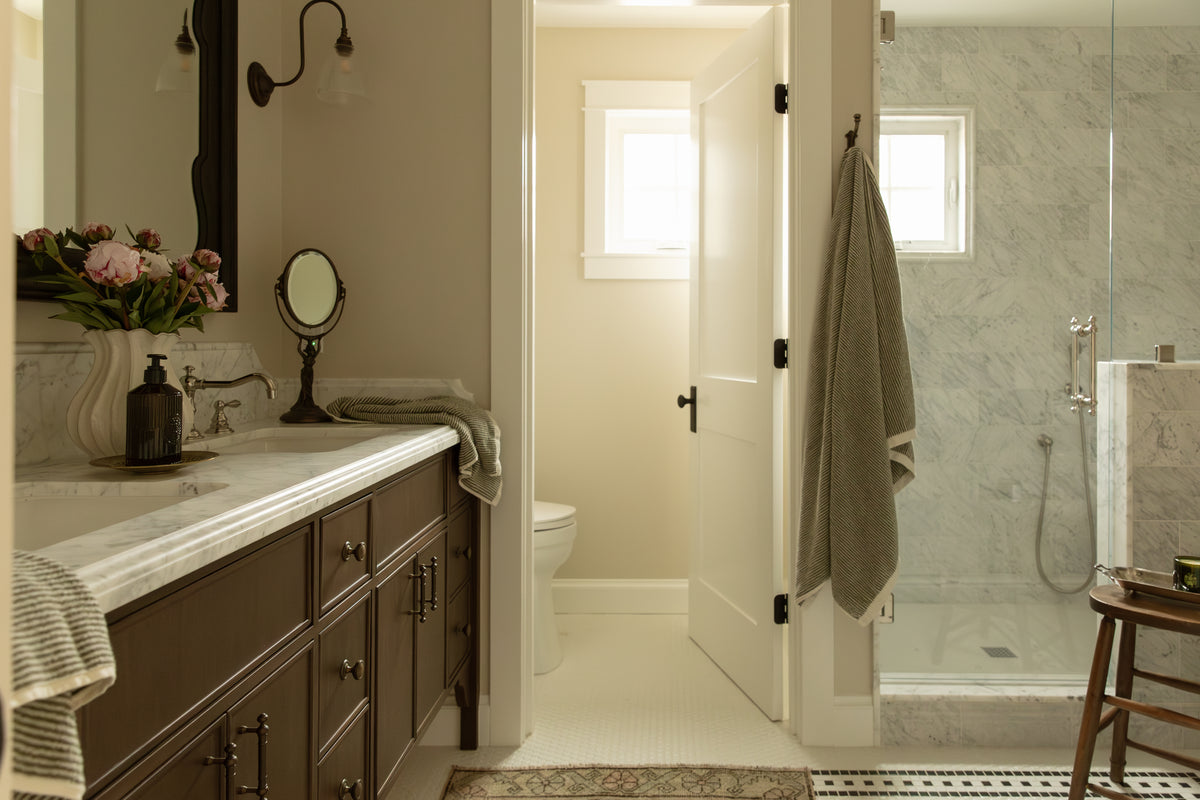 Freestanding white soaking tub with traditional exposed brass telephone faucet against a white marble tile wall with chair rail trim.
