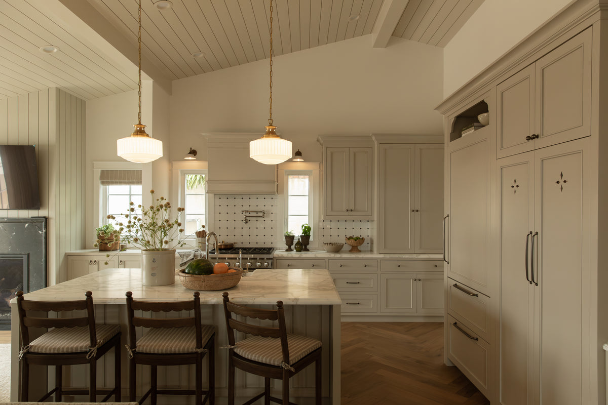 Open-concept Craftsman kitchen in Seal Beach featuring a marble island with wooden counter stools, brass milk-glass pendant lights, and light gray cabinetry.