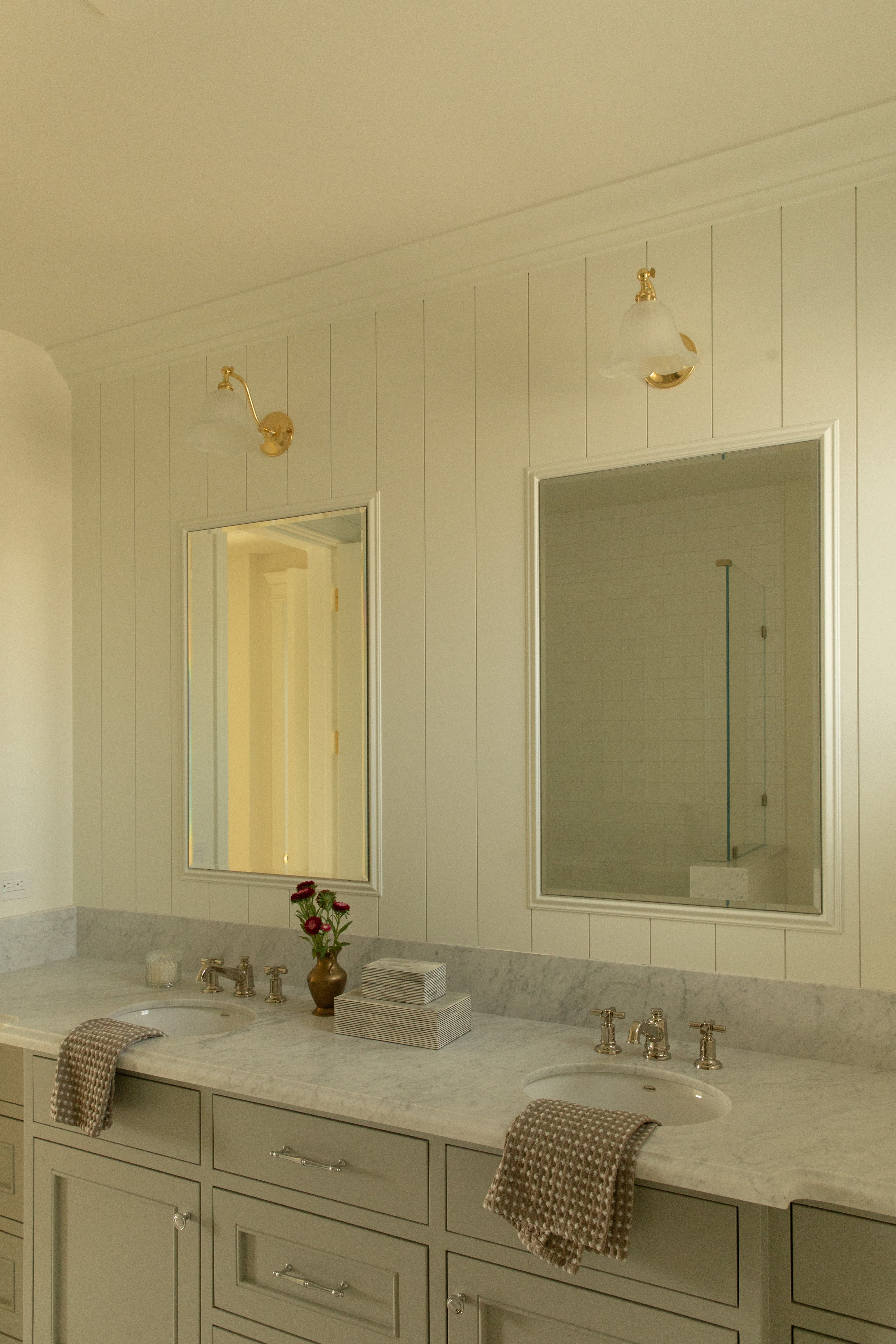 Wide view of a custom light pigeon colored bathroom double vanity featuring dual rectangular mirrors, brass wall sconces, and white vertical paneled walls designed by a Seal Beach designer.