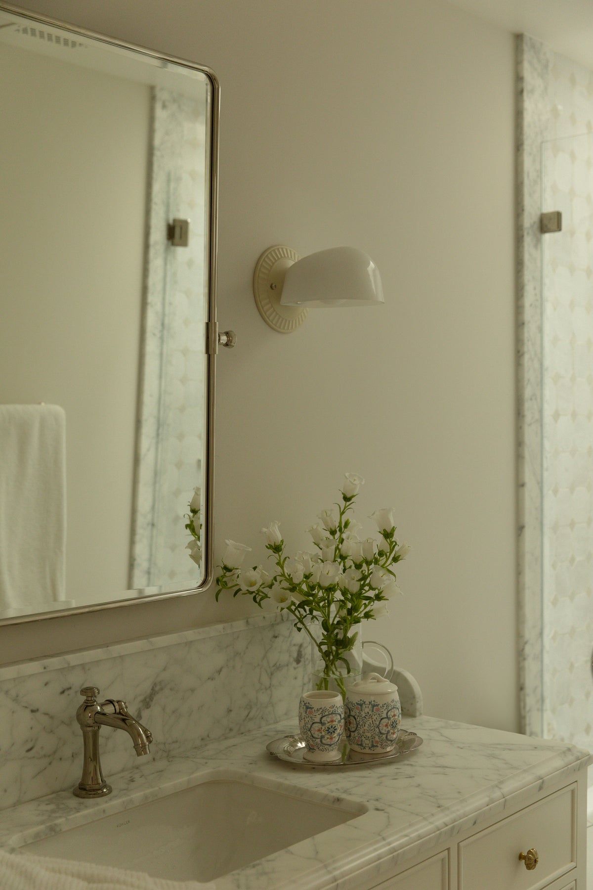 Hand-detailed bathroom  vanity with a polished marble countertop, polished nickel bridge faucet, and curved wall sconce in a full-scale high-end home rebuild. 