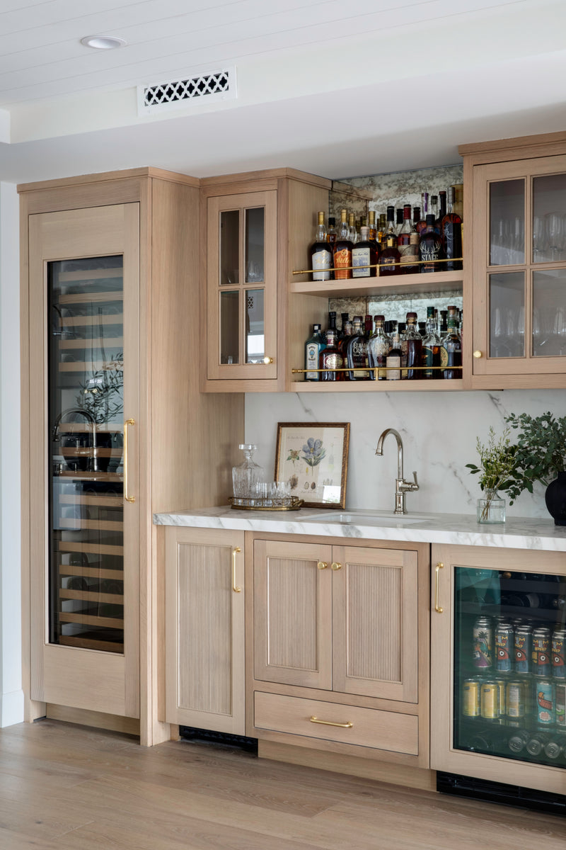 Custom-built home bar in Old Town Seal Beach featuring light white oak fluted cabinetry, integrated wine and beverage refrigerators, and elegant marble countertops.