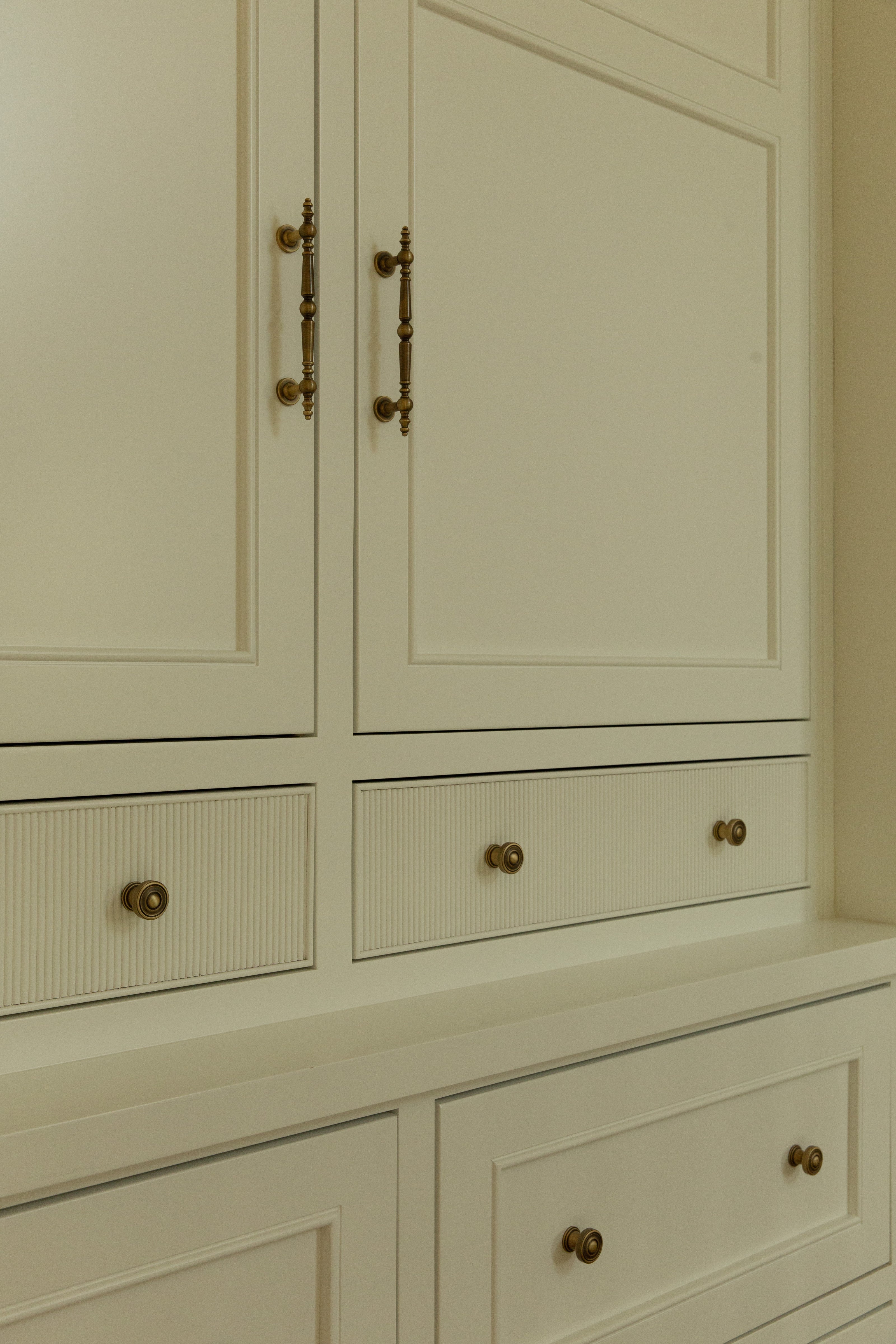 Close-up of custom white hallway linen cabinets in an Orange County remodel, featuring brass drop pulls on the upper doors and brass knobs on the fluted wood drawer fronts.