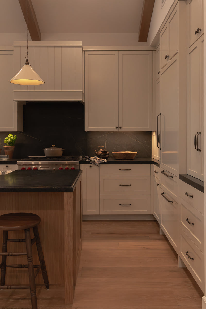 Detail shot of custom kitchen cabinetry designed for a Seal Beach remodel, featuring panel-ready appliances, deep drawers with dark bronze pull hardware, a custom wood range hood, and dramatic dark slab countertops.