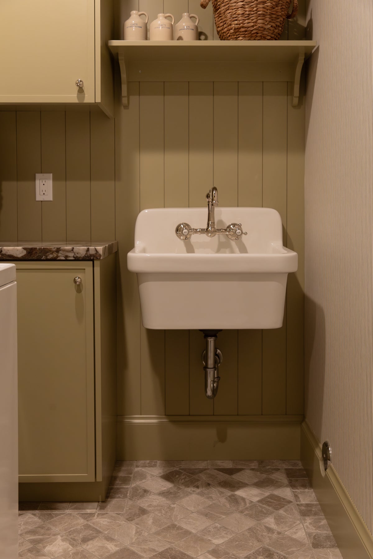 High-end utility laundry room featuring an olive green vertical paneling wall, wall-mounted cast iron sink, and marble checkerboard flooring. 
