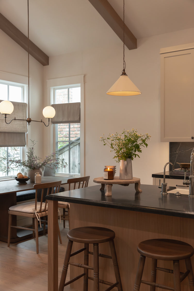 View of a remodeled bungalow kitchen featuring a white oak island with dark slab countertops, wooden barstools, and a custom built-in dining nook framed by a vintage-style brass globe chandelier.