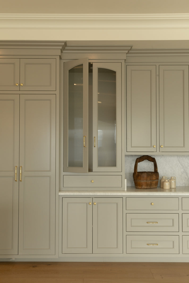 Custom olive green kitchen cabinetry featuring an integrated paneled refrigerator, brass hardware, and a countertop hutch with fluted glass doors resting on a marble counter in an Orange County home.