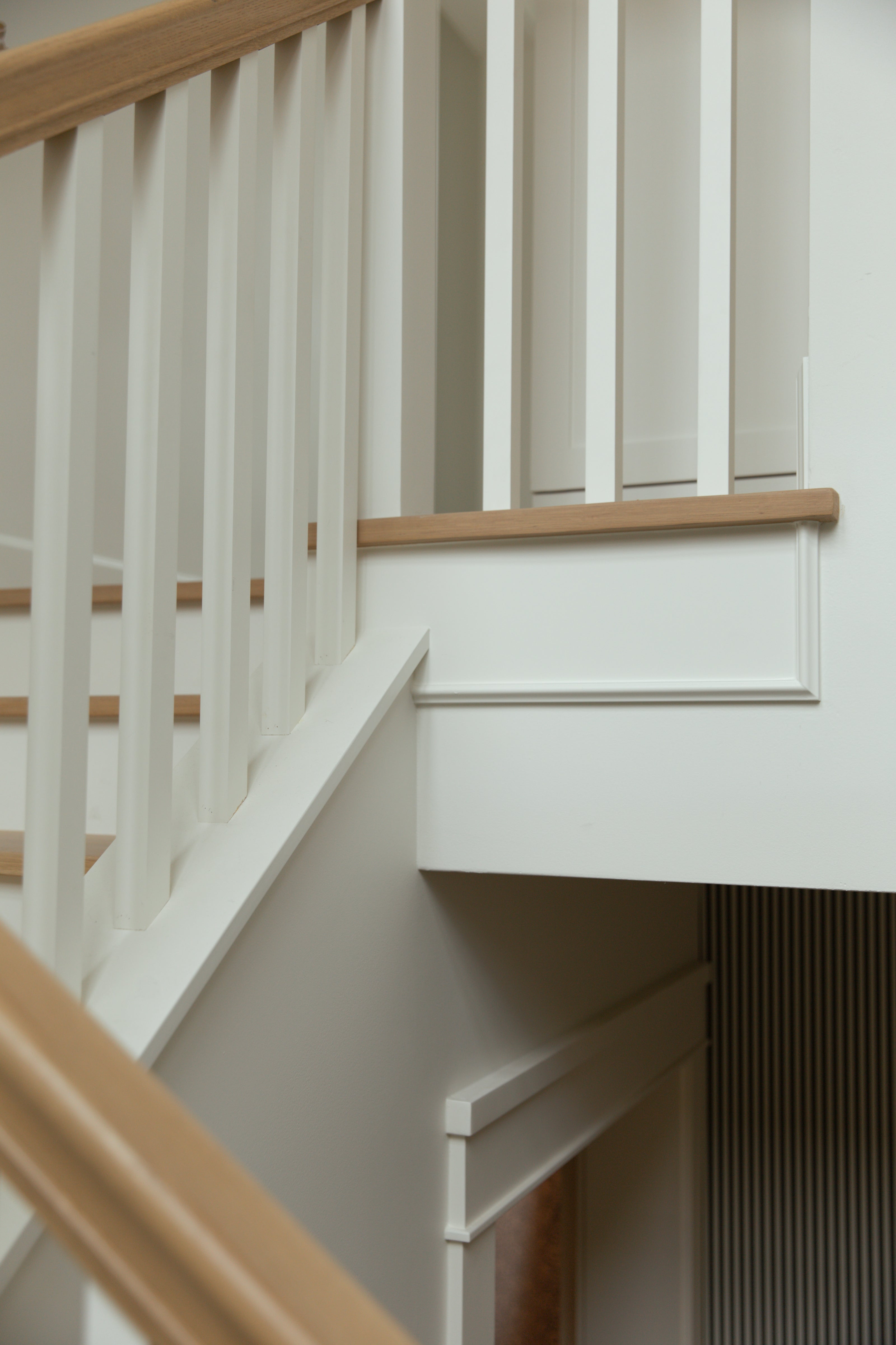 Close-up architectural detail of a staircase landing showing crisp white painted balusters, custom trim molding, and a smooth light oak handrail.