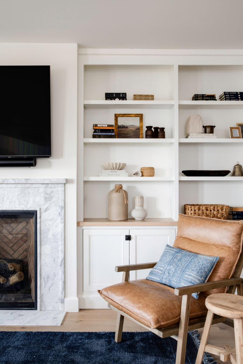 Custom white living room built-ins featuring open shelving styled with curated decor, adjacent to a marble fireplace and a leather accent chair.
