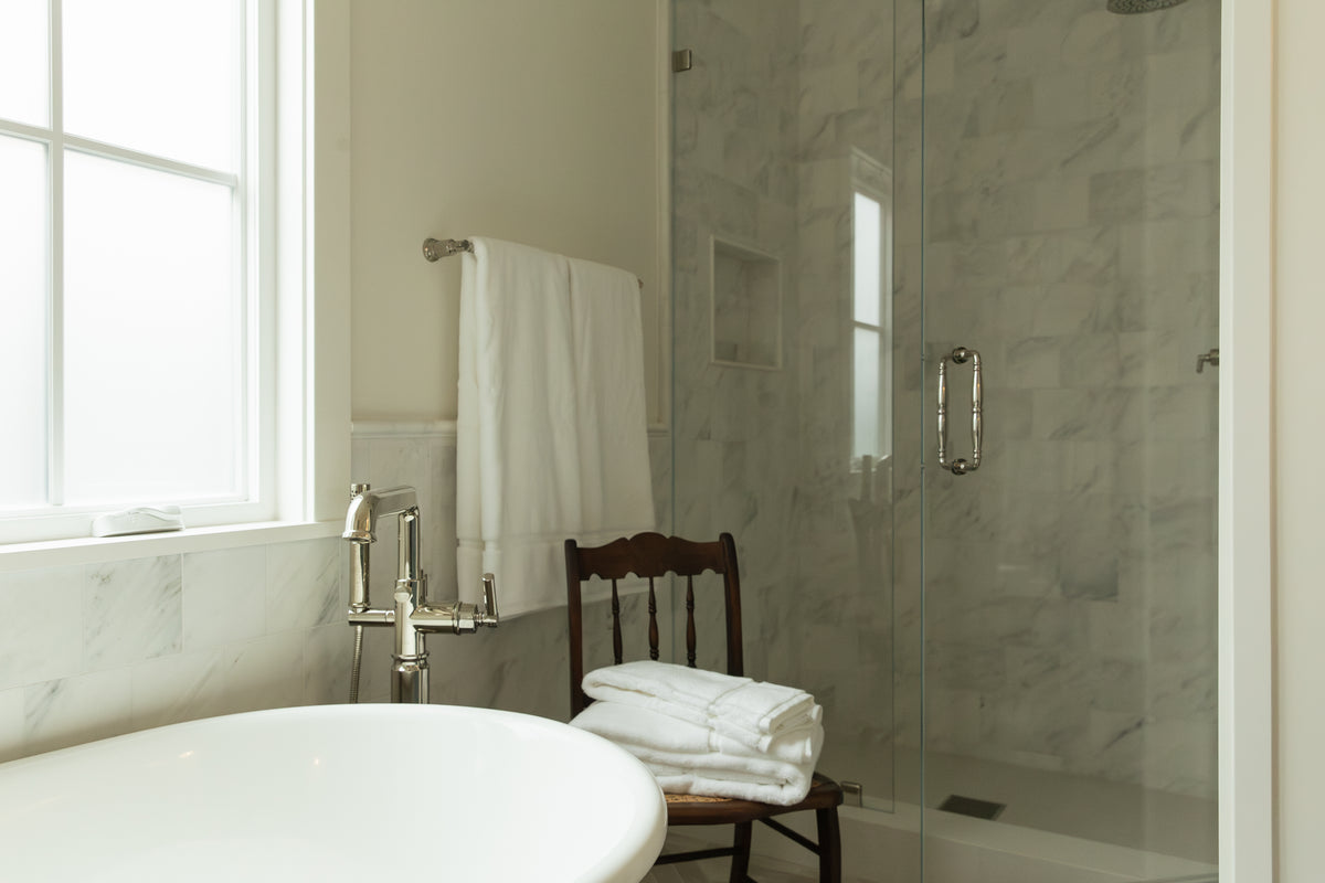 Orange County primary bathroom remodel showing a white freestanding soaking tub with a floor-mounted polished nickel tub filler, sitting adjacent to a seamless glass walk-in shower with marble tile walls.