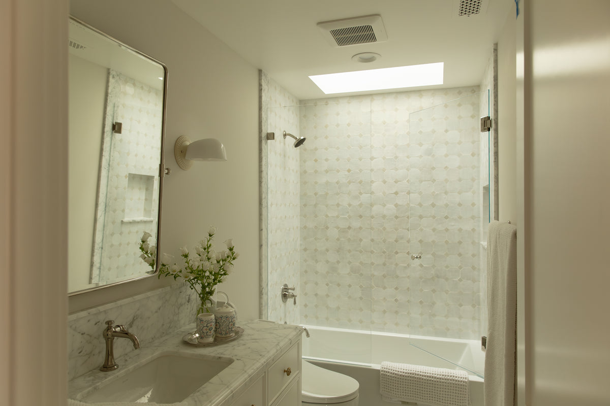 Bright primary bathroom remodel featuring a marble vanity, skylight, custom tile shower, and frameless glass door in Old Town Seal Beach, CA. 
