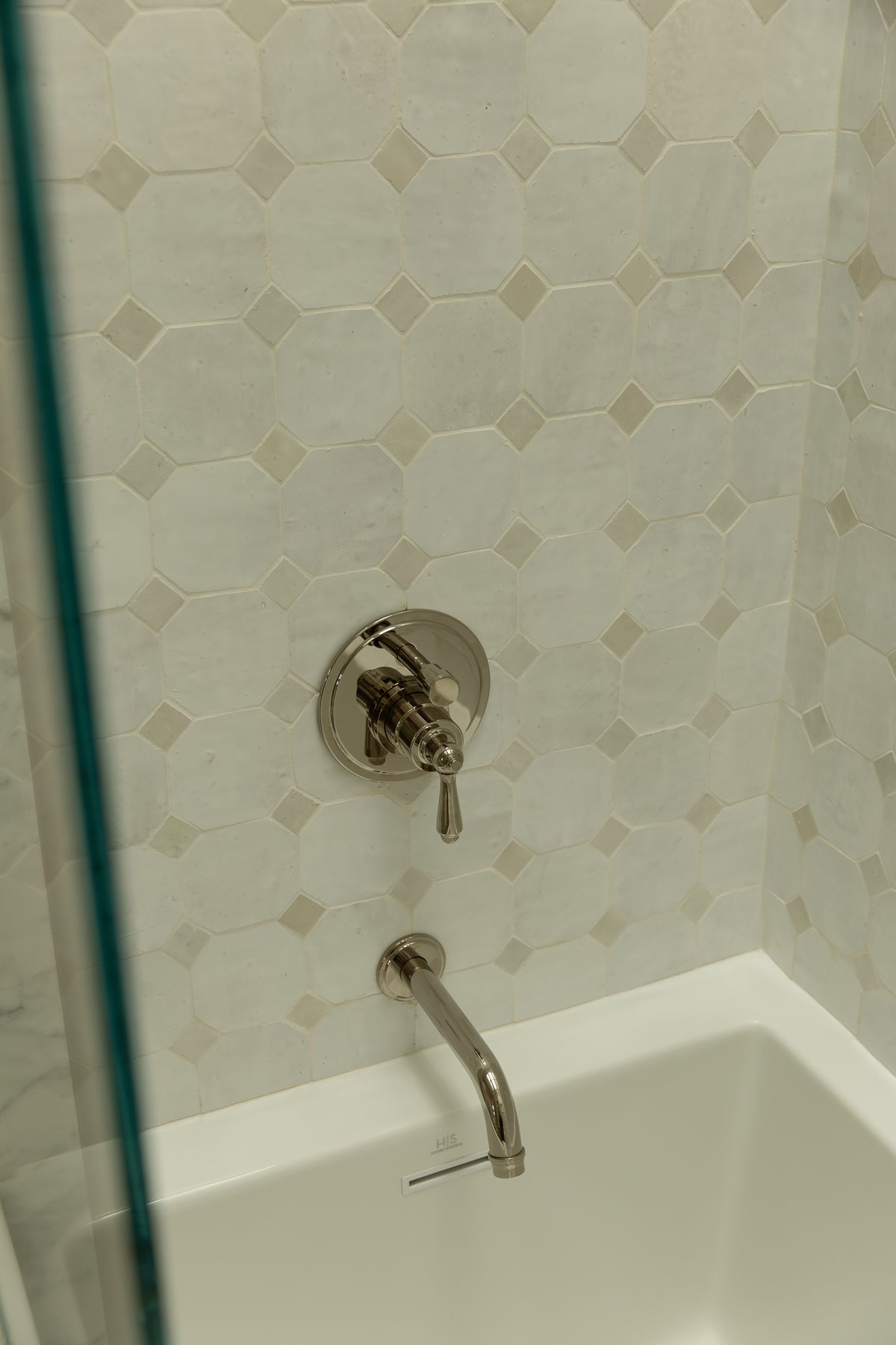 Custom shower and tub enclosure with mosaic marble wall tile detail and polished chrome fixtures designed by an Orange County interior design firm. 