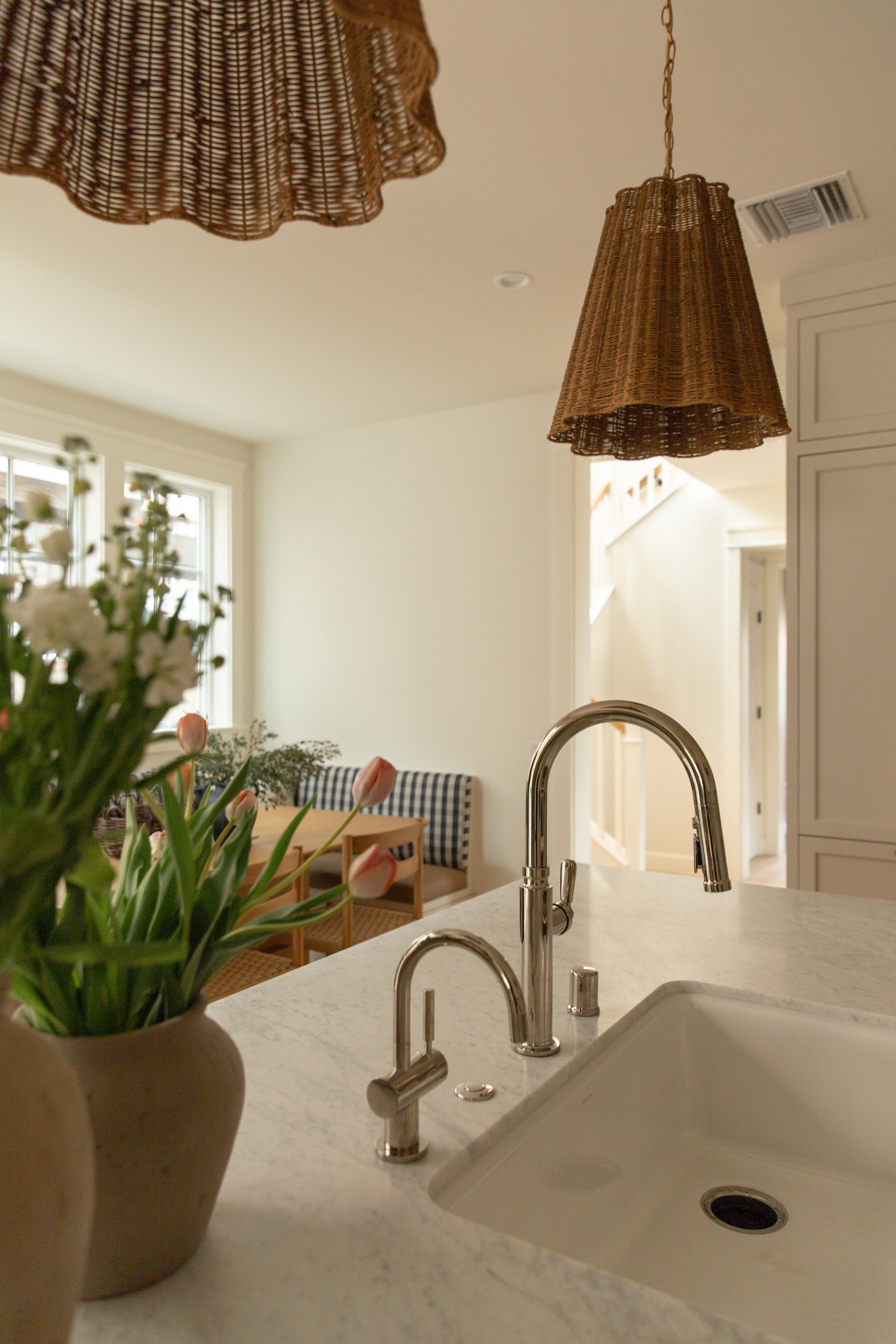 Close-up of a kitchen island featuring a white undermount sink, a polished nickel gooseneck faucet, and a woven rattan pendant light overhead.
