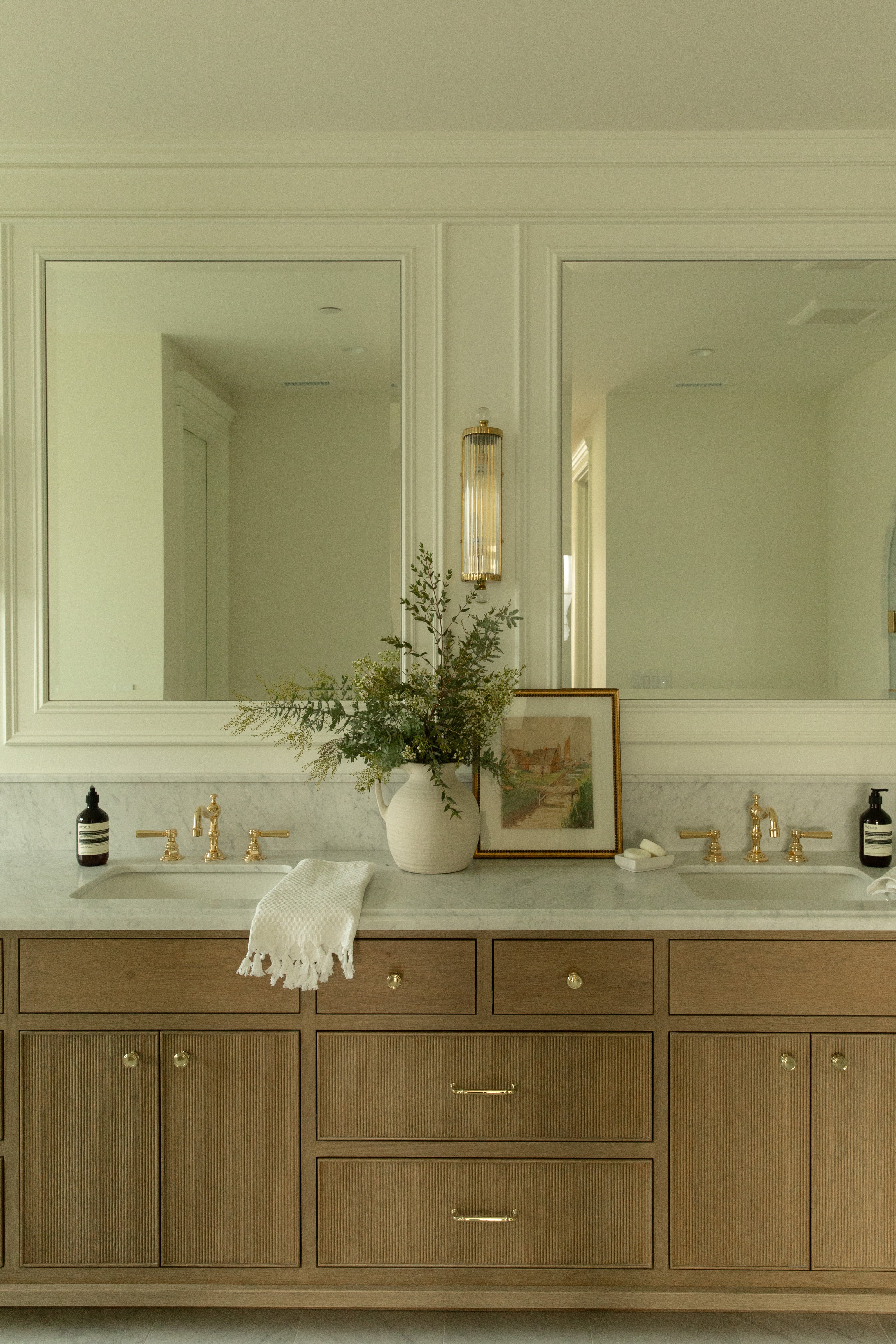 Wide view of a primary bathroom in a ground-up Seal Beach designer rebuild, featuring a custom fluted wood vanity with a marble top on the left and a large walk-in shower with an arched glass door in the center.
