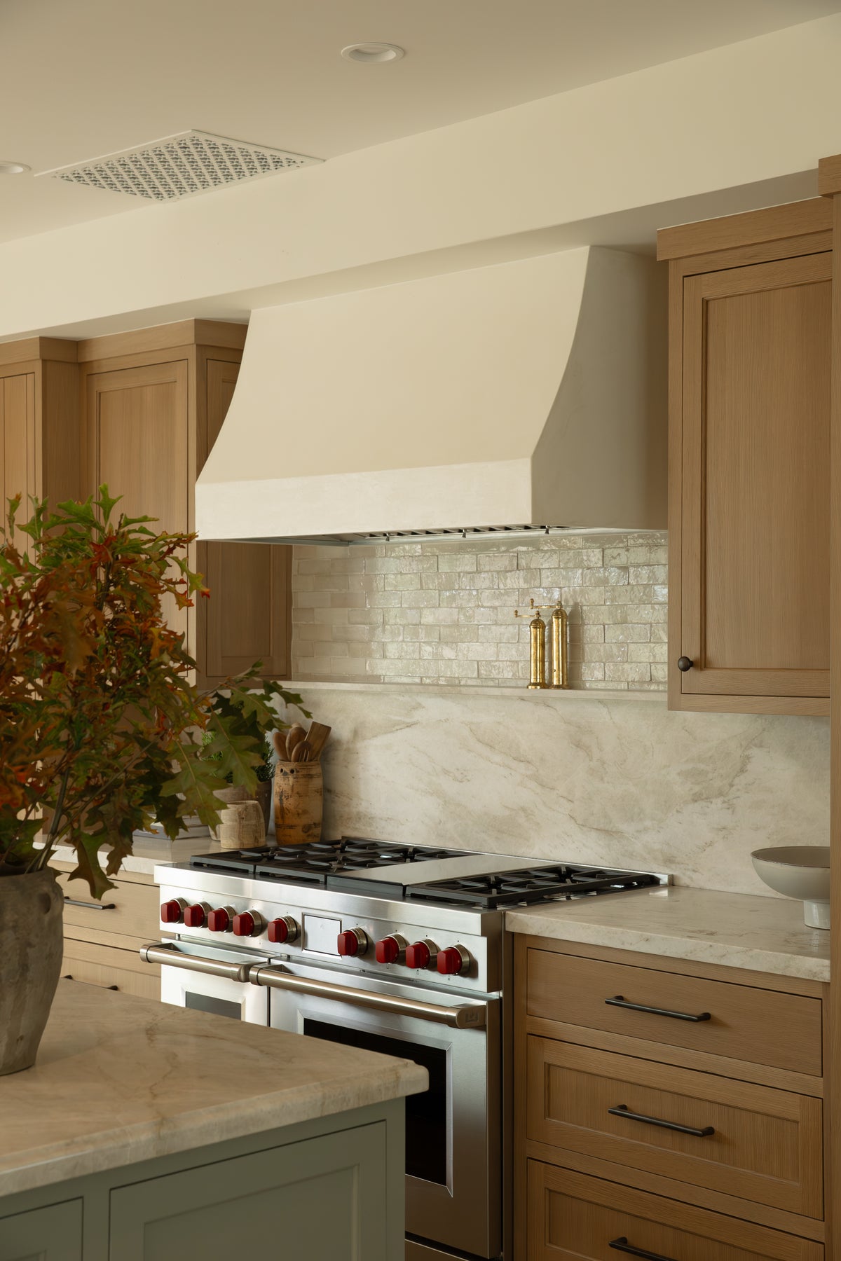 Angled view of a luxury kitchen cooking zone highlighting a narrow marble display ledge, a textured tile backsplash, and light oak shaker drawers finished with dark iron hardware.