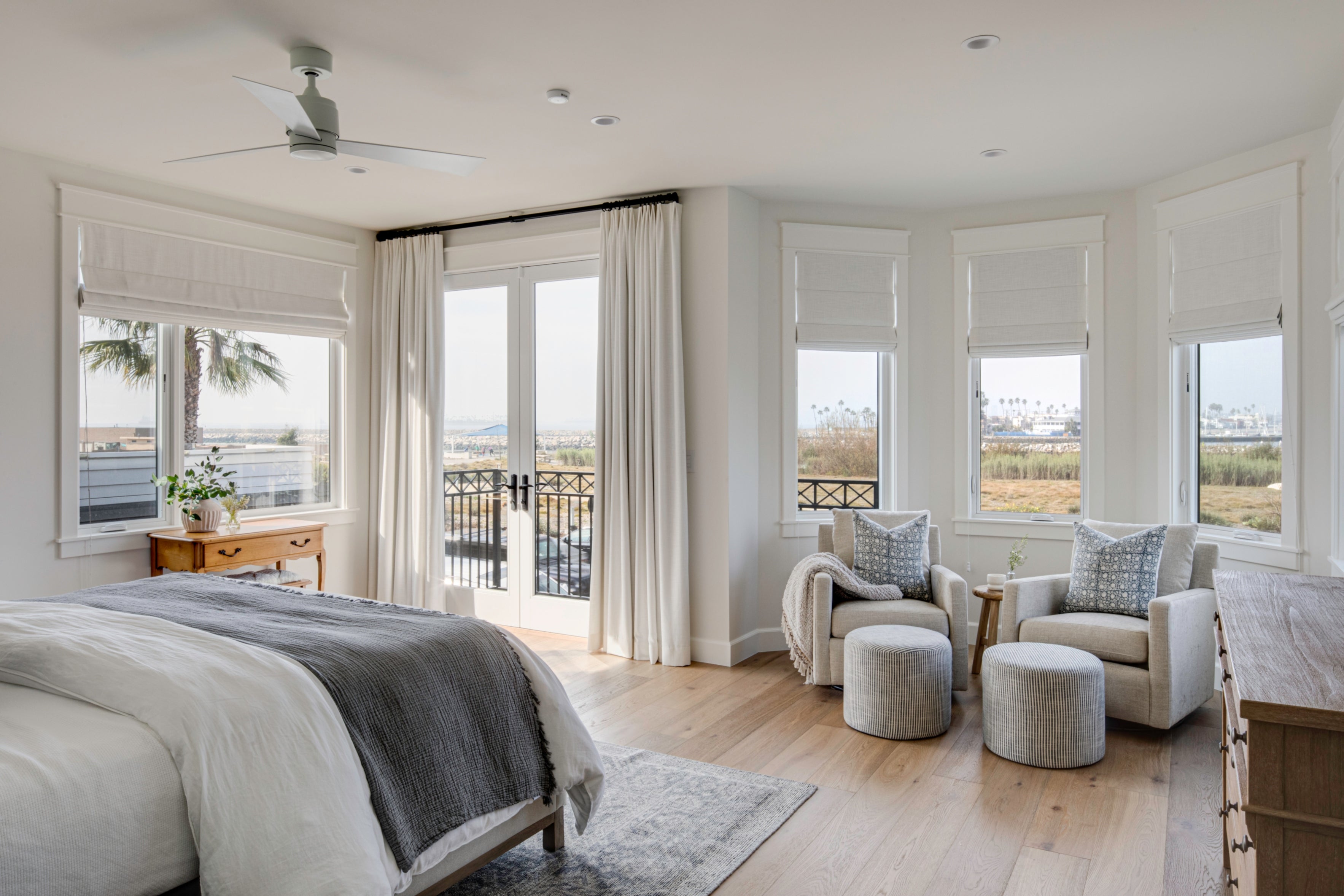 Custom coastal primary suite in Seal Beach by B Farm Design, showcasing a tranquil seating nook, floor-to-ceiling drapery, and sweeping views of the ocean.