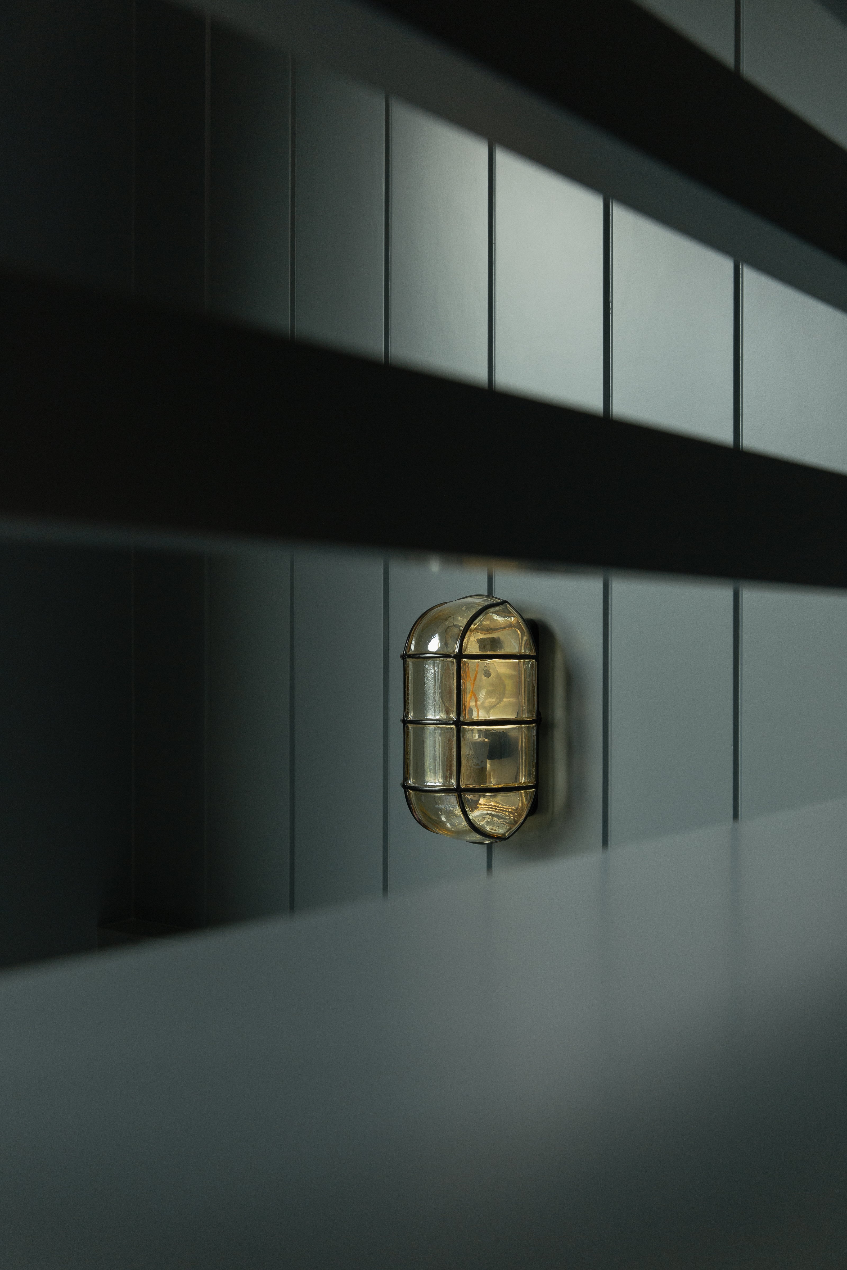 Detail shot of a vintage-inspired nautical brass bulkhead sconce mounted on dark vertical shiplap in a custom kids bunk room, viewed through the bed slats.