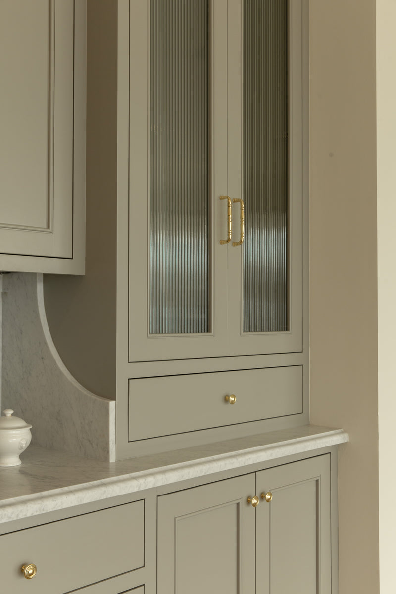 Close-up detail of custom kitchen cabinetry with reeded glass doors, brass handles, and a unique curved marble backsplash profile designed by a Seal Beach interior designer.