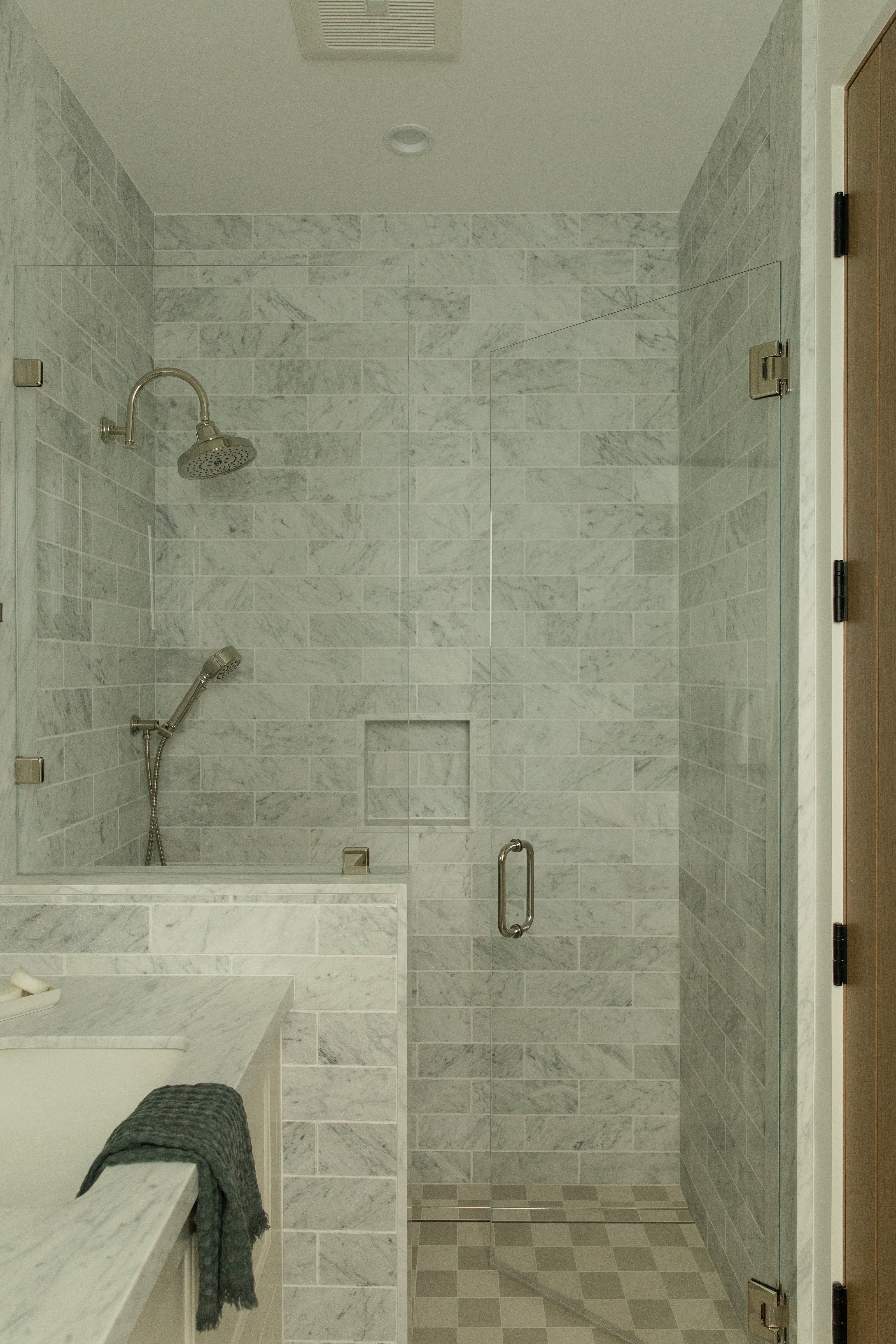 Looking through a doorway into a transitional guest bathroom featuring a white freestanding soaking tub, unlacquered brass fixtures, marble slab backsplash, and blue-grey floral wallpaper.