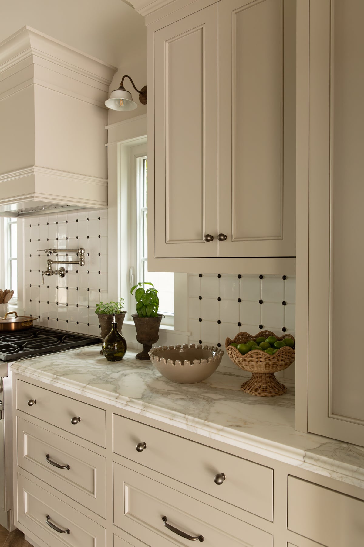 Angled view of light taupe shaker-style kitchen drawers, marble countertops, brass hardware, and decorative ceramic display bowls.