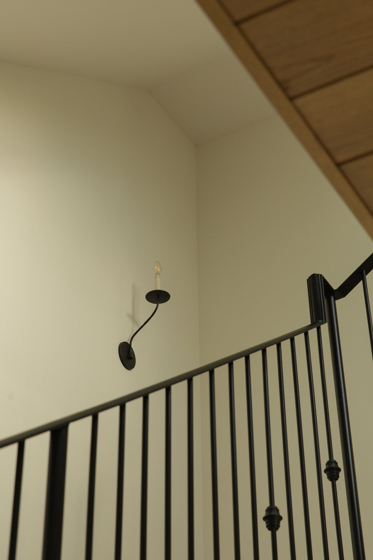 Looking up a transitional staircase with white paneled risers, light wood treads, and custom black wrought iron candle-style wall sconces on white walls.
