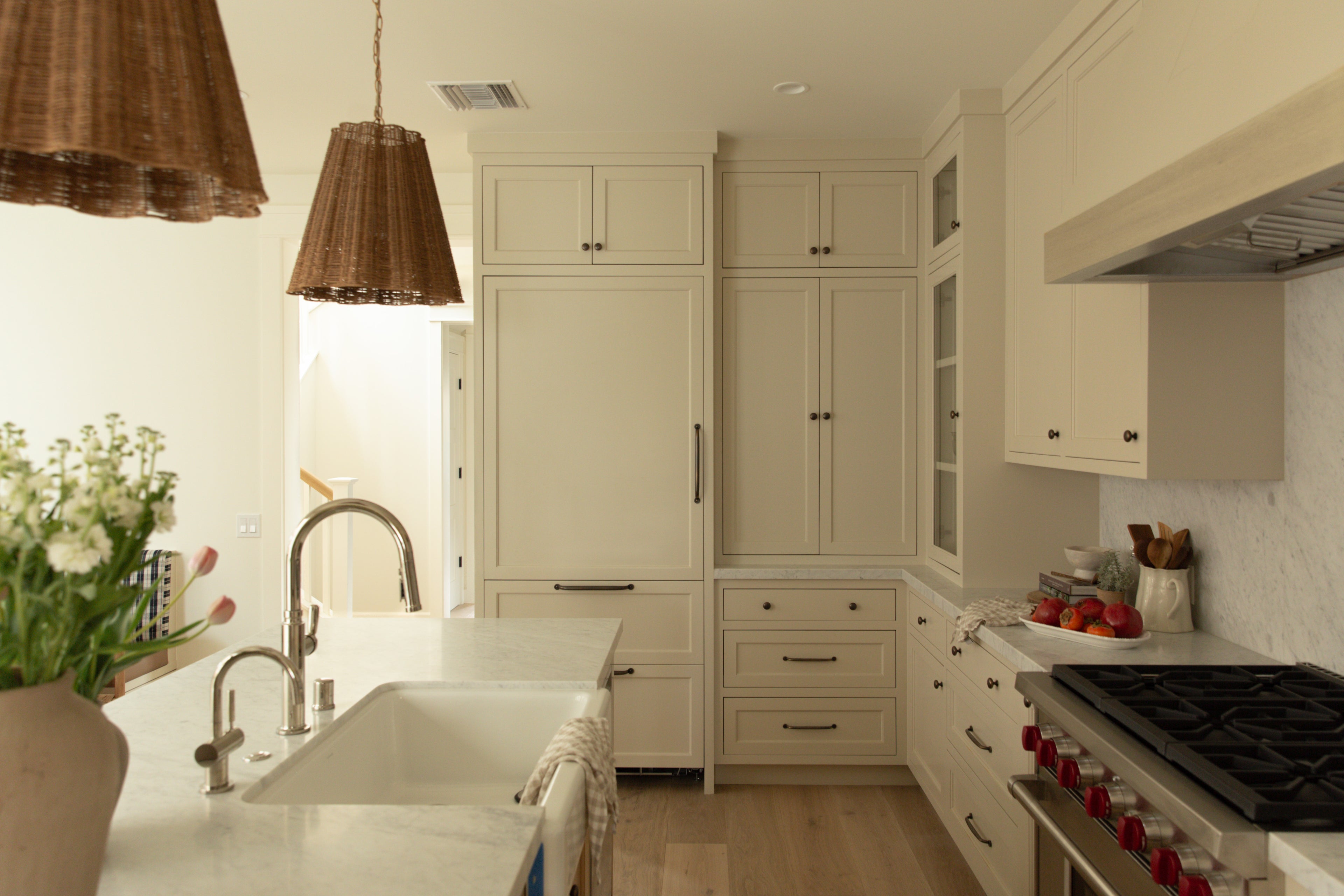 A stunning coastal farmhouse kitchen in Surfside, CA, featuring custom cream shaker cabinets, marble countertops, a panel-ready refrigerator, and a professional range.