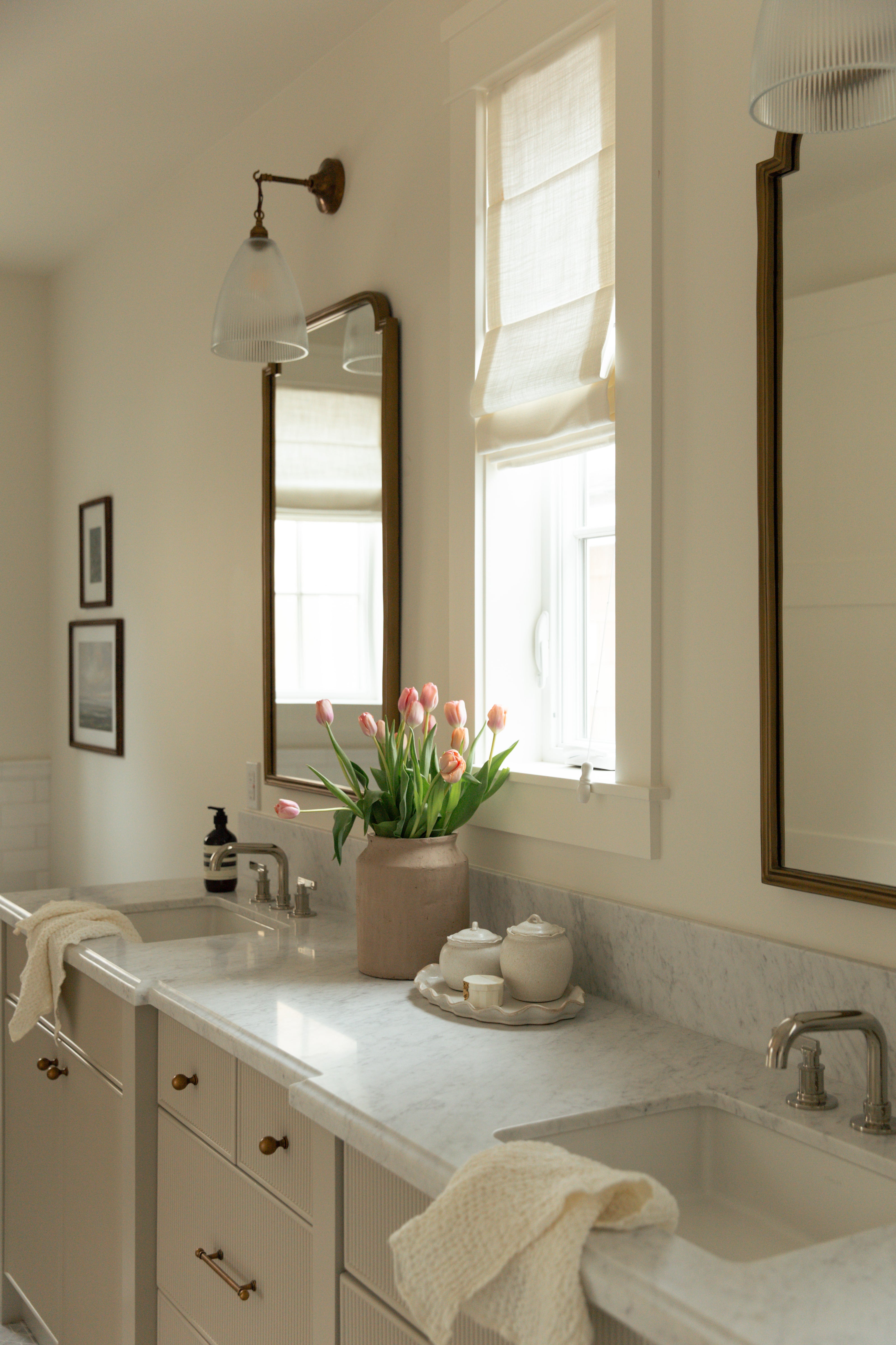 A luxurious primary bathroom in a Surfside custom coastal farmhouse, featuring a greige double vanity with reeded cabinetry, thick marble countertops, and warm brass mirrors.