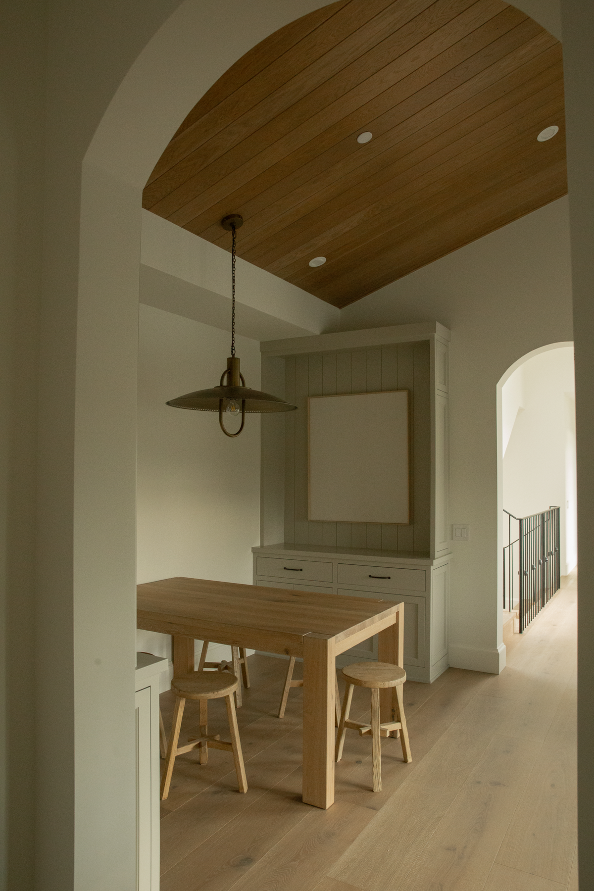 Dedicated art nook off the family room in a custom Seal Beach villa, showcasing built-in cabinetry, wide plank oak flooring, and a statement brass pendant light.