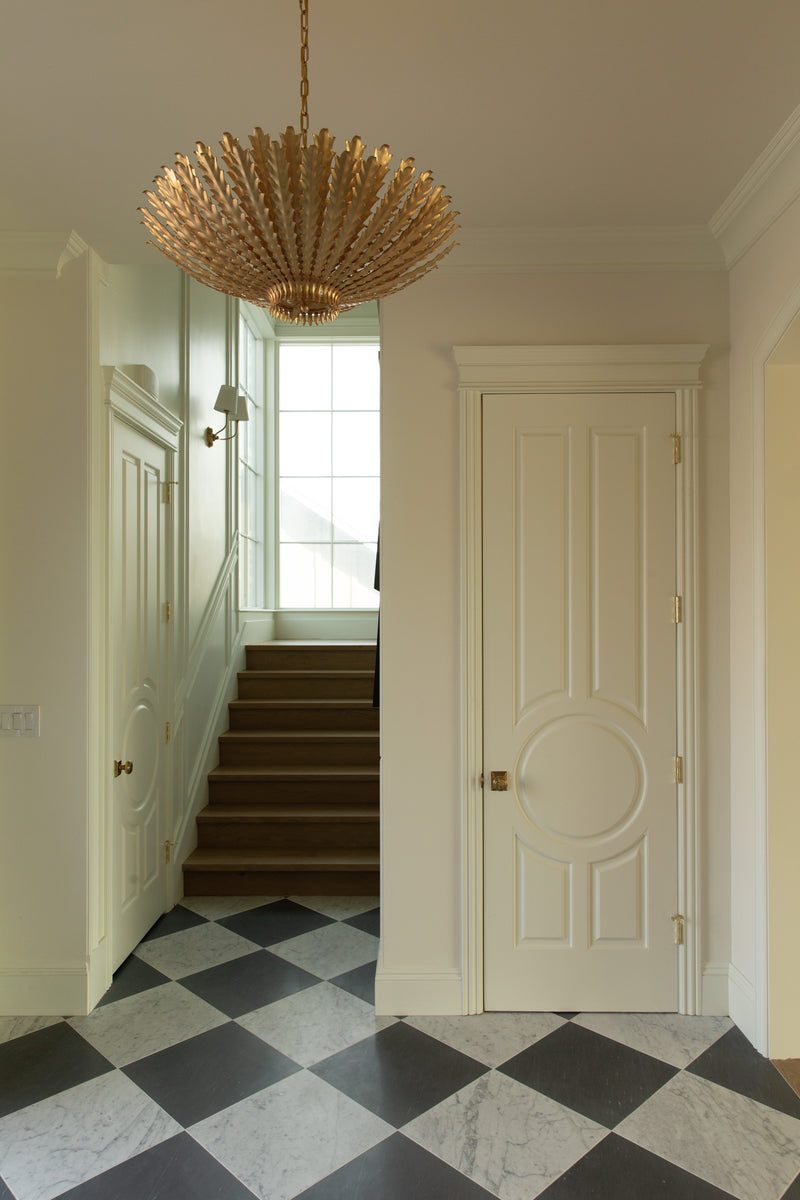 View of a classic entryway in a Rossmoor home rebuild featuring a black and white checkerboard marble floor, custom white doors with circular panel molding, a large gold leaf chandelier, and a light oak staircase.