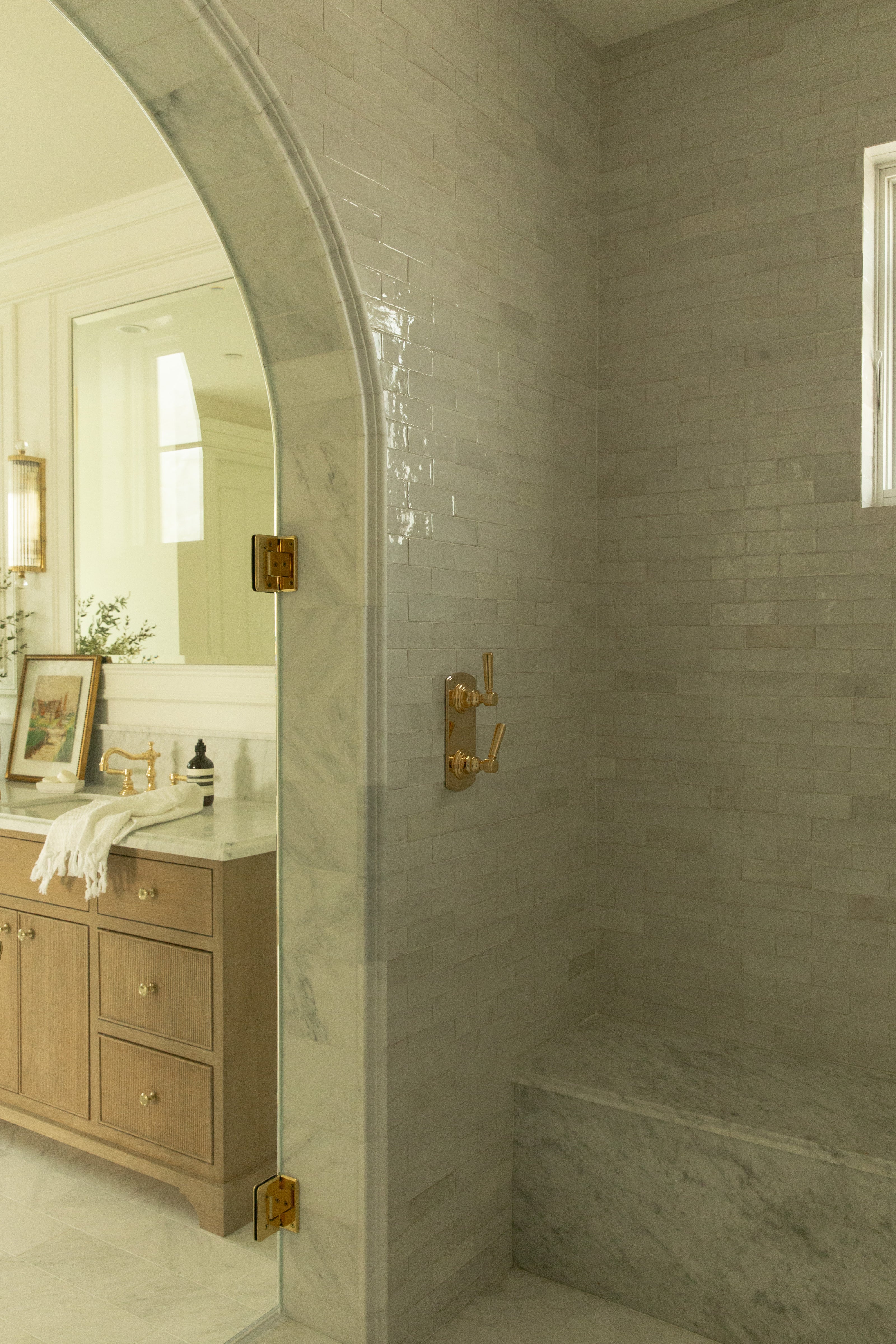 Arched glass shower door in a luxurious Orange County bathroom remodel, showing a marble threshold and a  custom wood double vanity beyond the glass shower door.