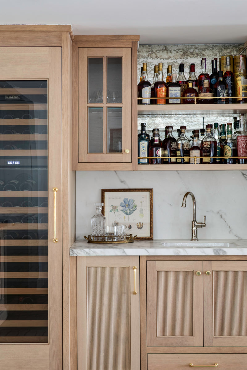 Custom white oak fluted cabinetry wet bar by B Farm Design featuring an integrated wine refrigerator, marble countertops, and open shelving.